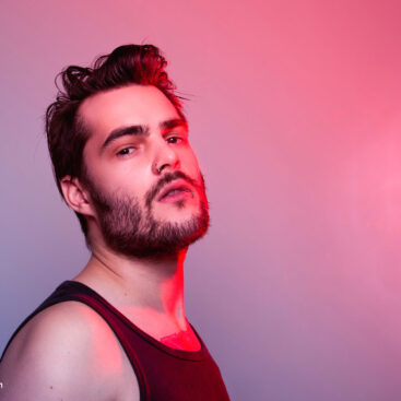 Portrait des stilvollen jungen Mannes im schwarzen Tanktop auf einem weissen Hintergrund, fotografiert