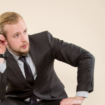 Stilvolle Mode Fotoshooting für den modernen Gentlemen im dunklen Anzug mit schwarzem Schuhe auf Stuhl sitzend